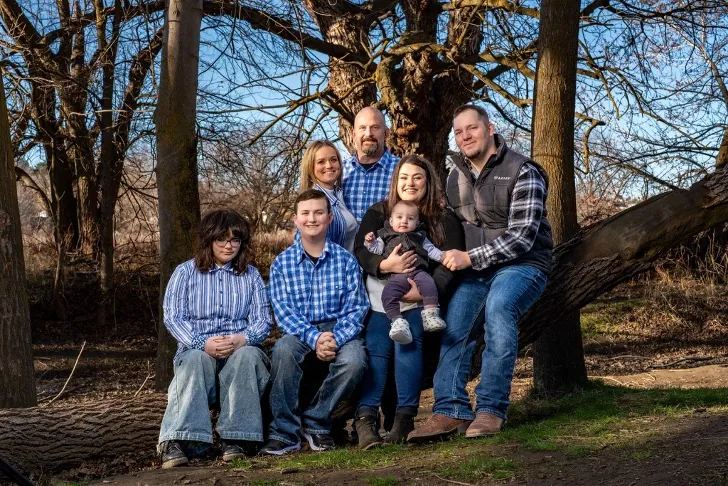 Chris Lee with his wife Julie, their children, son-in-law and grandchild seated on a fallen tree